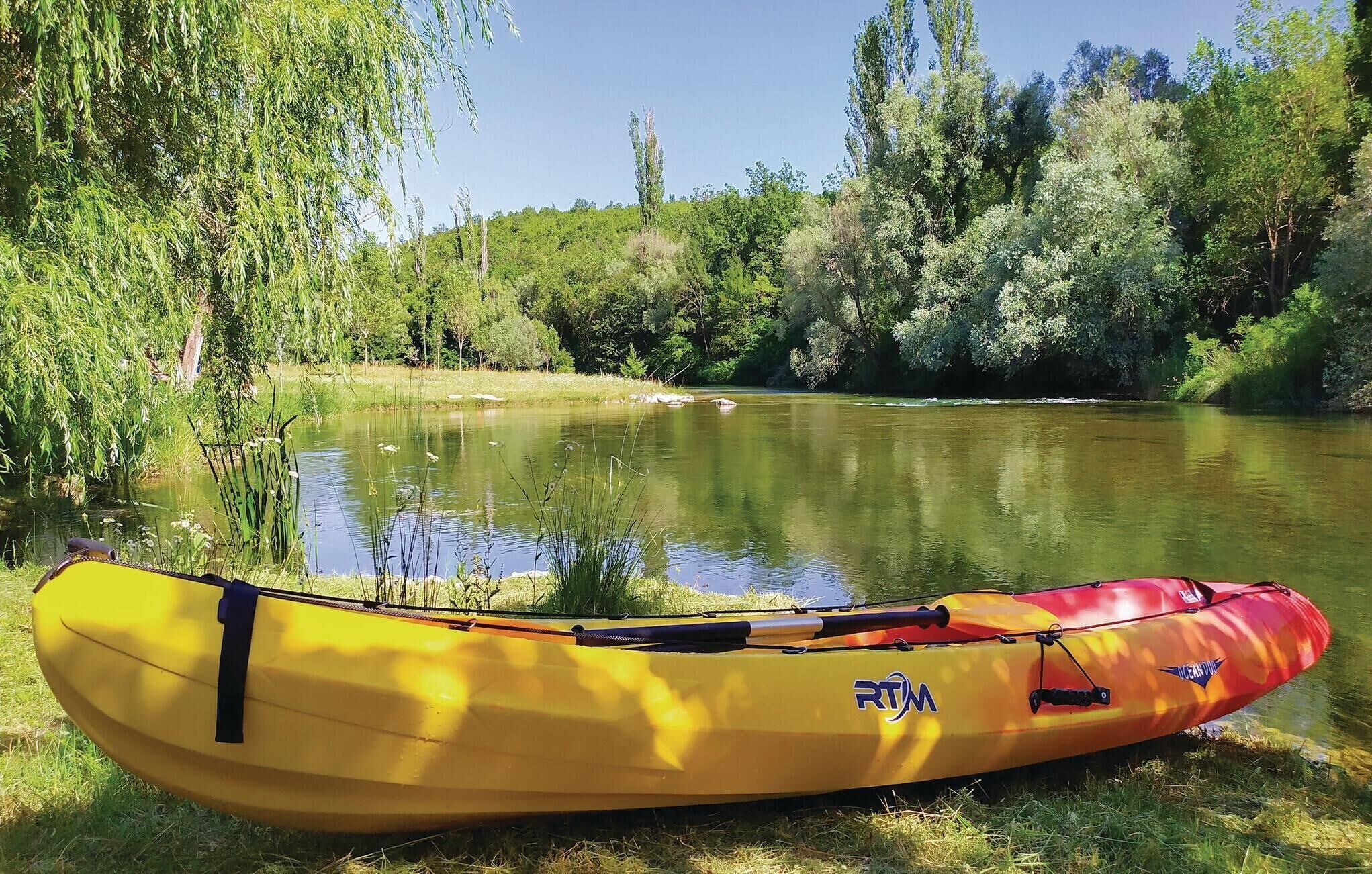 Kayak groc i vermell amb el nom de marca "PORTM" a un riu tranquil envoltat de vegetació exuberant.