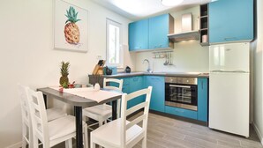 Une cuisine avec des meubles de rangement bleus, un réfrigérateur blanc et un coin repas avec des chaises et une table blanches.