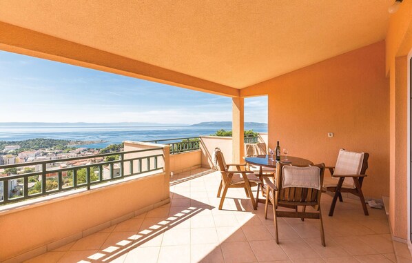 En balkon med et bord og stole, udsigt til havet og en by i baggrunden.