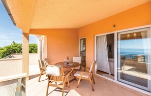 En balkon med et bord og stole, en skydedør og havudsigt.