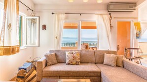 Una sala de estar acogedora con un amplio sofá modular, una mesa de centro de madera y vistas al mar a través de amplios ventanales.