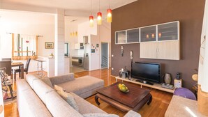 Una sala de estar moderna con un televisor de pantalla plana, una mesa de centro de madera y un sofá. Se ve un área de cocina al fondo.