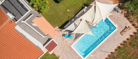An aerial view of a property with a swimming pool, outdoor seating, and a well-maintained garden.