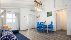 A spacious living area with a blue sofa, a dining table with blue chairs, and a hanging light fixture.