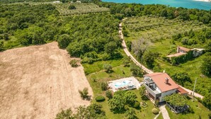 An aerial view of a property with a swimming pool, a modern house, and surrounding greenery.