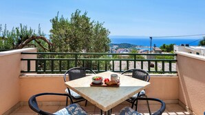 A balcony with a table and chairs, overlooking a coastal view with trees and buildings. - 3 bedroom beautiful apartment in Makarska (Makarska)