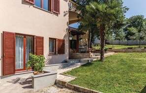 Ein Haus mit überdachter Veranda, einer kleinen Sitzgelegenheit im Freien und einem gepflegten Rasen.