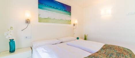 A hotel room with a bed, a nightstand, a vase with flowers, and a painting of a beach scene.