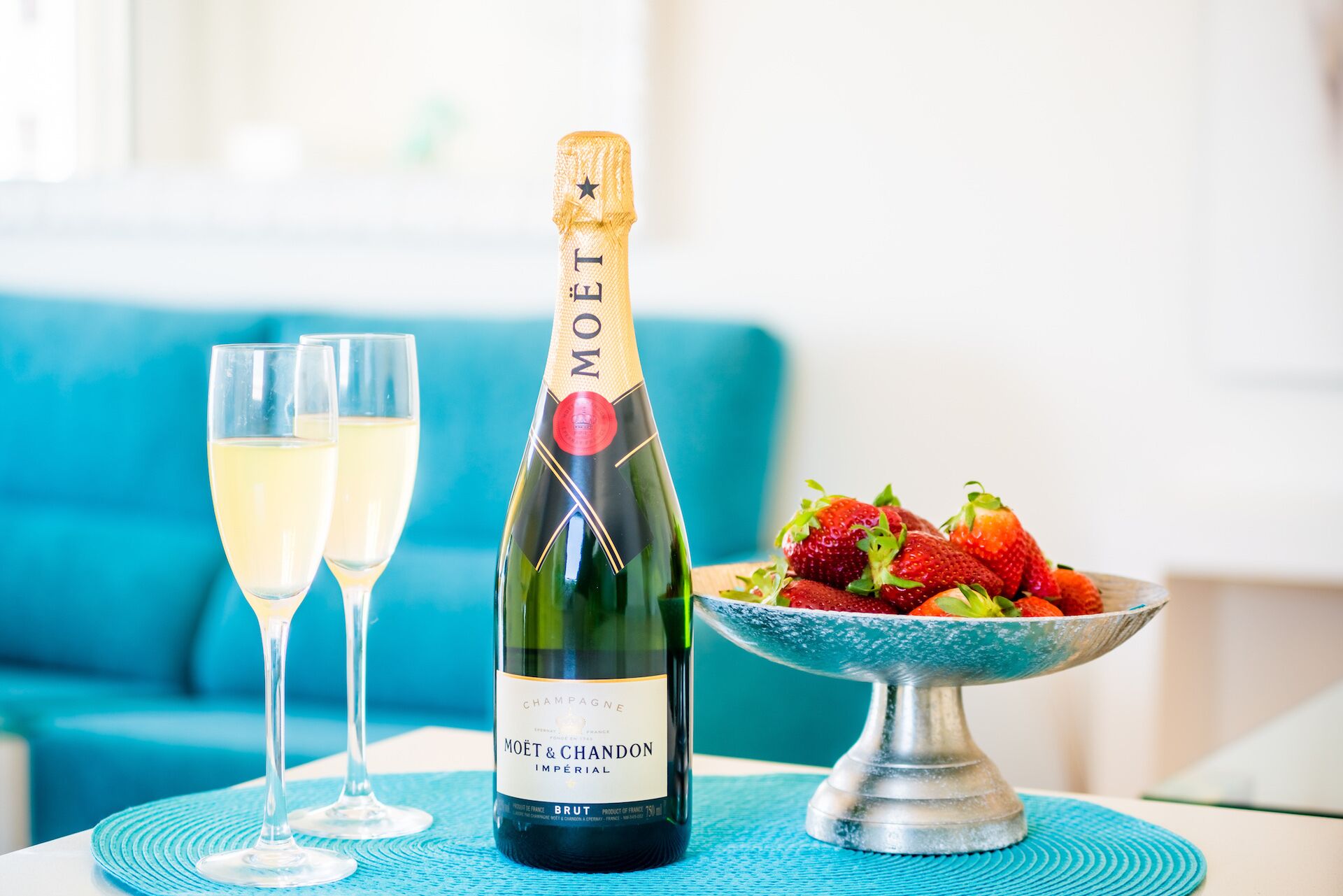 A bottle of Moët & Chandon champagne, two glasses of champagne, and a bowl of strawberries on a table.