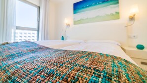 A hotel room with a bed, a painting on the wall, and a window with curtains.