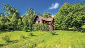 A two-story wooden house with a sloped roof, surrounded by a lush green lawn and dense trees. - Awesome home in Breze with WiFi (Breze)