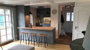 A modern kitchen with a central island, bar stools, pendant lighting, and a visible clock on the wall.