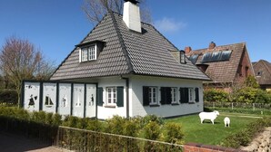 A traditional house with a steep gabled roof, a chimney, and a fenced yard with sheep.