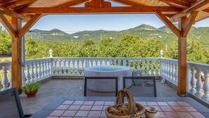 A covered outdoor area with a hot tub, a table with a basket, and a view of green hills. - Beautiful apartment in Hreljin with WiFi (Hreljin)