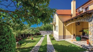 A courtyard with a stone pathway, a yellow building with a tiled roof, and a stone wall. - Beautiful apartment in Hreljin with WiFi (Hreljin)