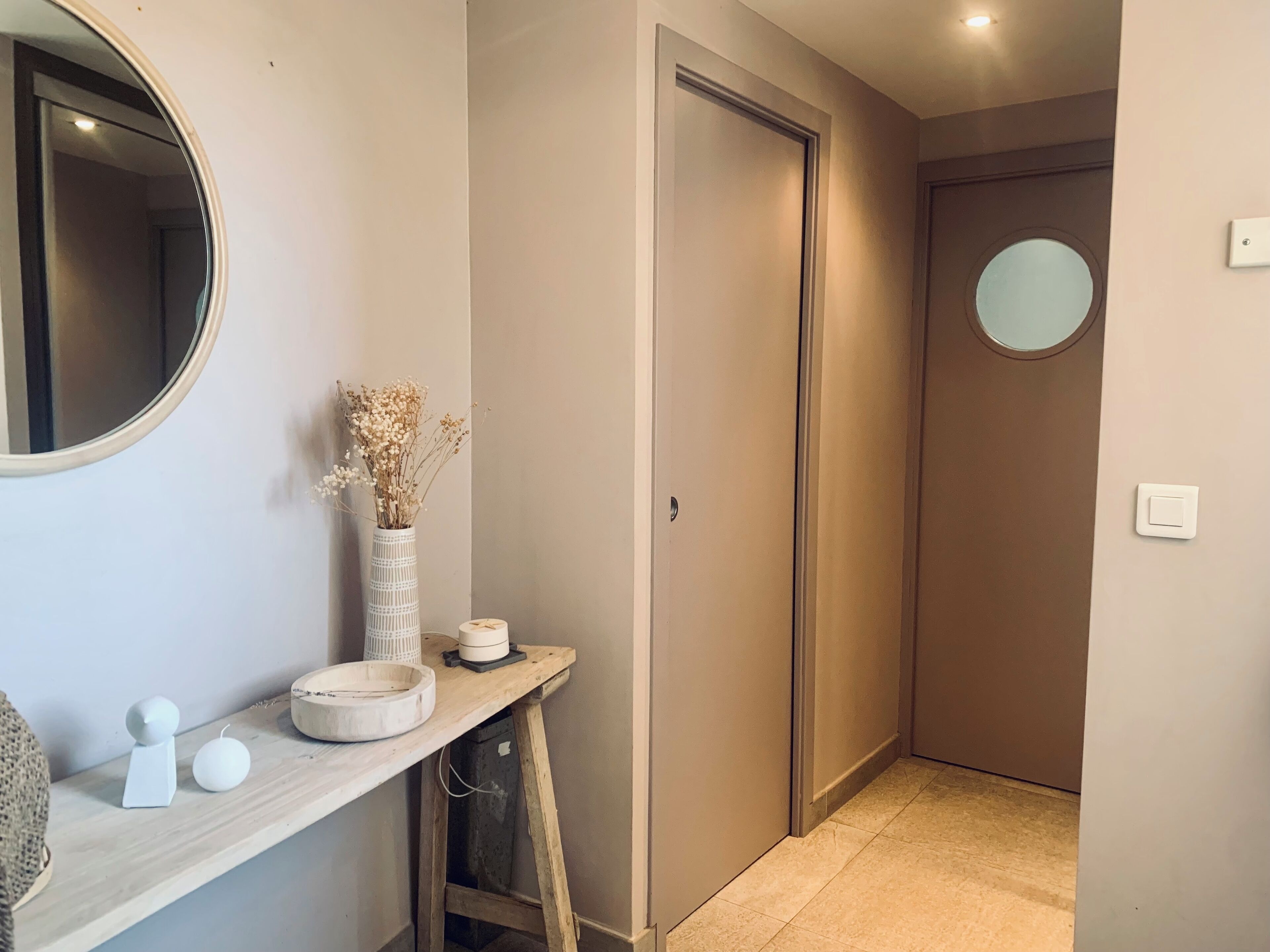 A hallway with a wooden console table, a mirror, a vase with dried flowers, and a door.