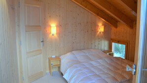 Een slaapkamer met een houten plafond, een groot bed, twee nachtkastjes en twee wandlampen.