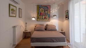 Un dormitorio con una cama, dos mesitas de noche, aire acondicionado, radiador y un cuadro abstracto grande en la pared.