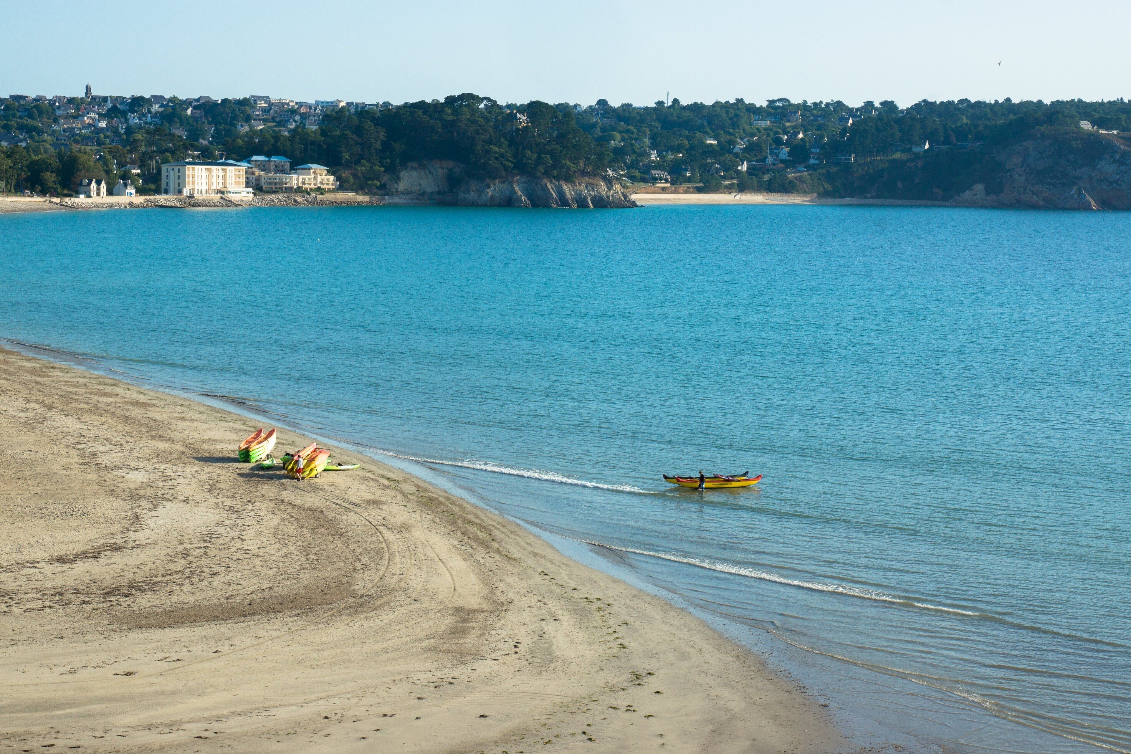 A beach with a clear view of the sea, a sandy shore, and a distant town.