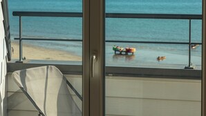 Un balcón con vista a la playa, una silla y una mesa.