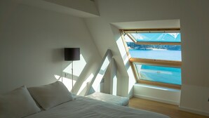 Un dormitorio con una cama, televisor montado en la pared y tragaluz con vista a un cuerpo de agua.