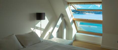 A bedroom with a bed, a wall-mounted TV, and a skylight overlooking a body of water.