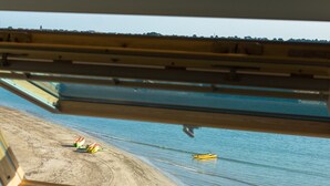 Vista desde una habitación con tragaluz, con vistas a una playa y un bote amarillo, con algunas personas.