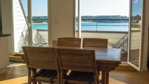 Un área de comedor con una mesa y sillas, un ventanal corredero que da a un balcón con vista al mar y un puente.