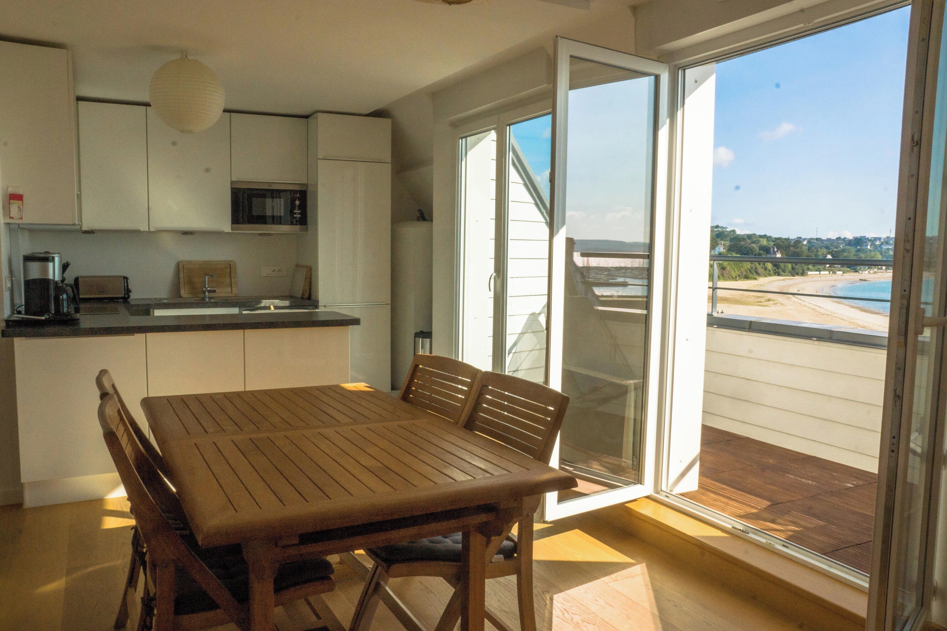 A kitchen with a dining table and chairs, a microwave, and a view of the beach through a sliding glass door.