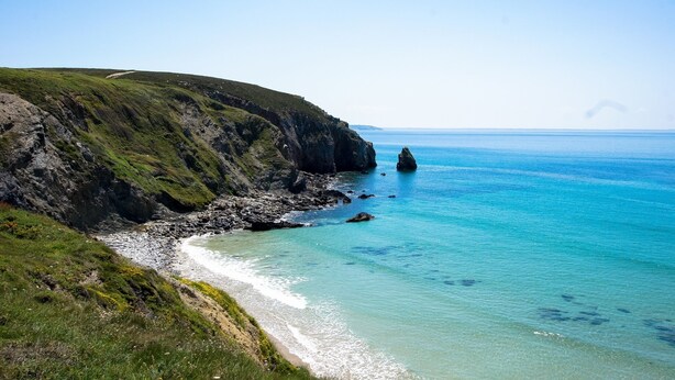 Un paisaje costero con un acantilado rocoso y mar azul cristalino.