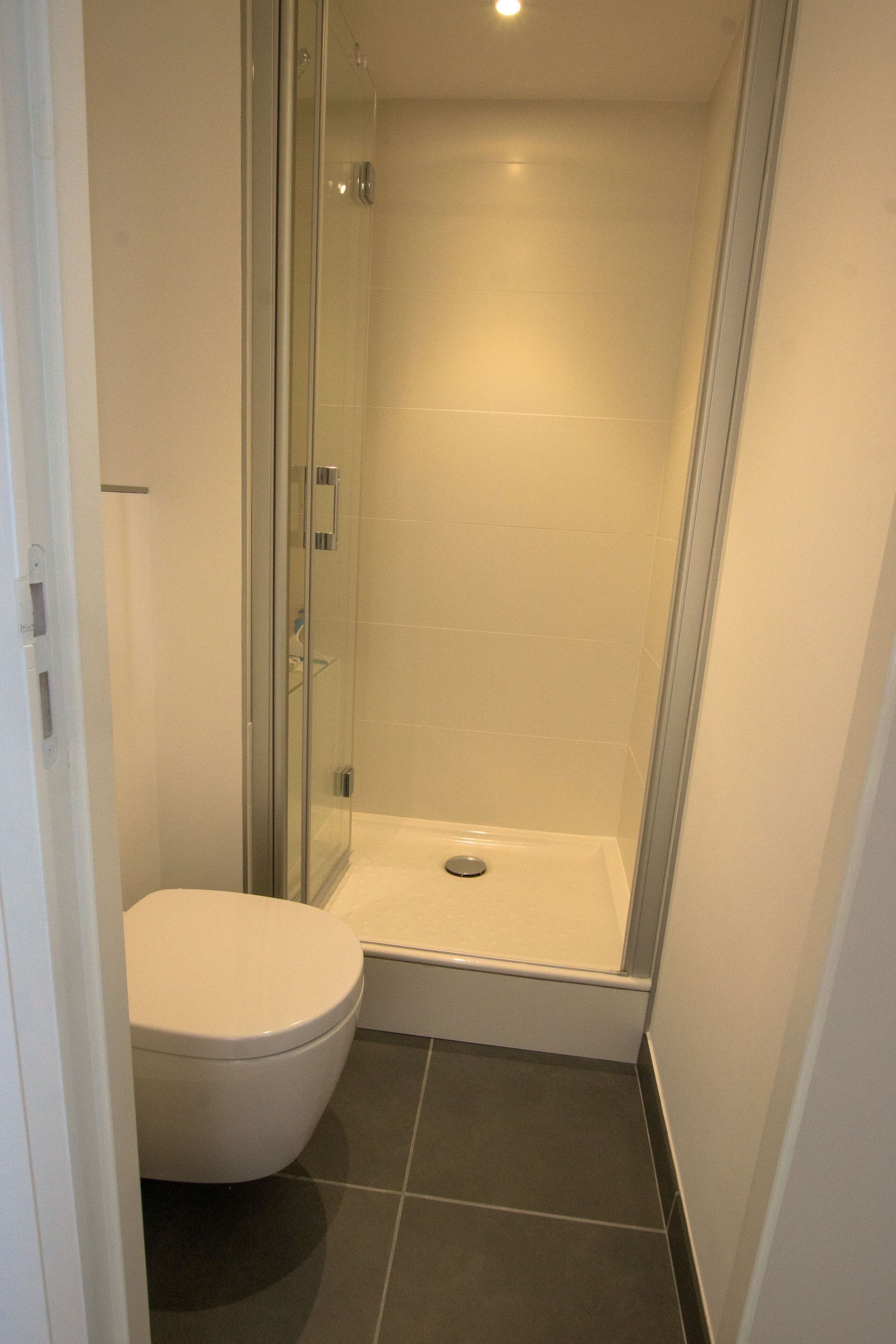 A compact bathroom with a glass-enclosed shower, a white toilet, and dark tiled flooring.