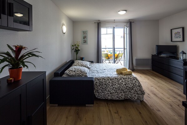 A modern bedroom with a bed, a desk, a dresser, and a potted plant.