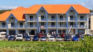 Un hôtel à plusieurs étages, avec un toit rouge et des balcons bleus. Plusieurs voitures sont garées devant.