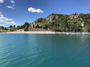 Ett kustområde med en strand, båtar och en bergig kulle med byggnader.