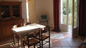 A dining area with a table and chairs, a television on a stand, a cabinet, and a sliding glass door leading to a balcony. - EDONIAA vacation rentals in the heart of the Bay of Somme (Quend)