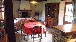 A cozy dining area with a red tablecloth, wooden chairs, a fireplace, and a television. - EDONIAA vacation rentals in the heart of the Bay of Somme (Quend)