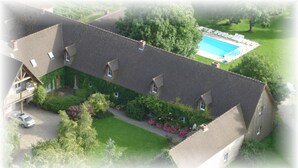 An aerial view of a residential property with a swimming pool, multiple houses, and a car parked in the driveway.