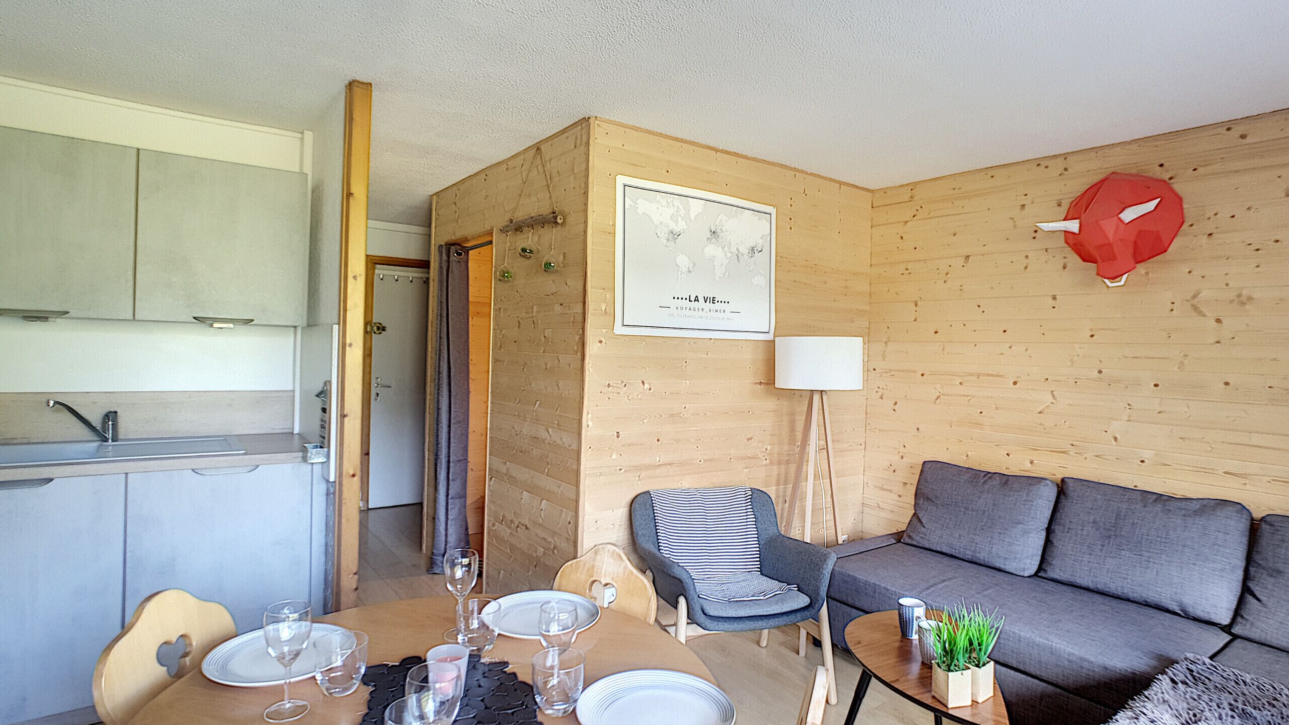 Un espacio habitable compacto con kitchenette, una zona de comedor con mesa dispuesta para dos, un sofá y una silla.