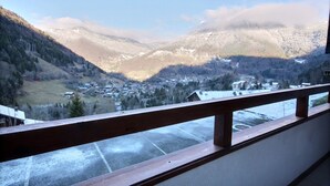 A view from a balcony with a wooden railing, overlooking a valley with snow-covered mountains and a small town below. - DAILLE  S18 - 4 PERS - WIFI - SWIMMING POOL ACCESS - SAINT JEAN D'AULPS RESORT - NEAR MORZINE (Saint-Jean-d´Aulps)