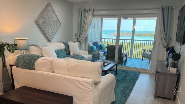 Ein Wohnzimmer mit einem weißen Sofa, einem Holztisch, einer dunklen Kommode und Meerblick durch große Schiebetüren.