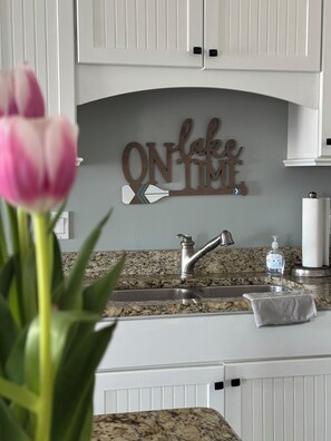 A kitchen with white cabinets, a granite countertop, a stainless steel sink, and a decorative sign above the sink.