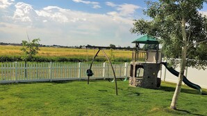 Ein Spielplatz mit Schaukel und Rutsche, umgeben von einem weißen Zaun und einer grünen Wiese.