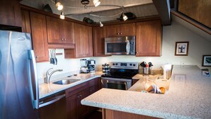 Eine moderne Küche mit Holzschränken, Edelstahlgeräten, einer Granitarbeitsplatte und Pendelleuchten.