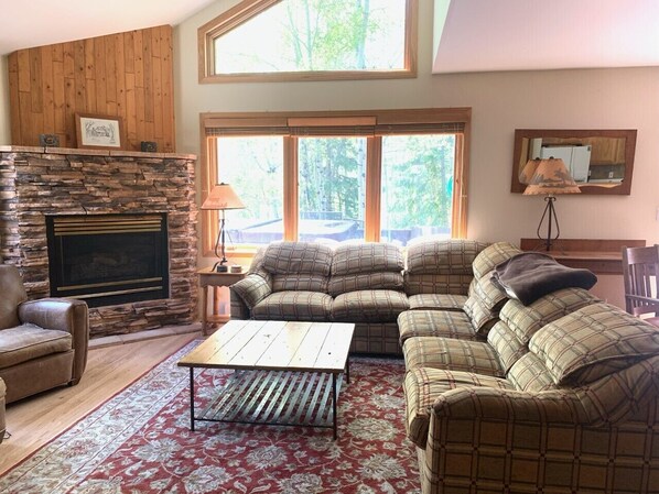 A cozy living room with a stone fireplace, large windows, a sofa set, and a coffee table. - Burgundy Chalet -- Private Mountain Getaway! BCA - 48176 (Silverthorne)