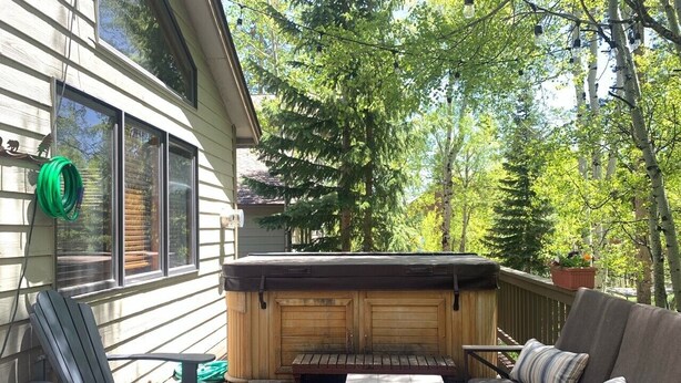 A deck with a hot tub, wooden deck, outdoor furniture, and a house with windows.