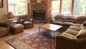 A living room with a stone fireplace, leather furniture, and large windows.