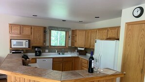 A kitchen with wooden cabinets, a microwave, a refrigerator, and a wine bottle.