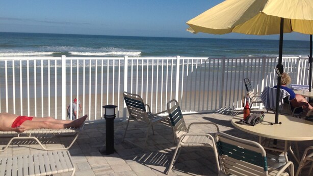 A beachside patio with chairs, a table, and an umbrella, overlooking the ocean.