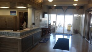 A hotel lobby with a reception desk, a dining area, and a view of the outside.