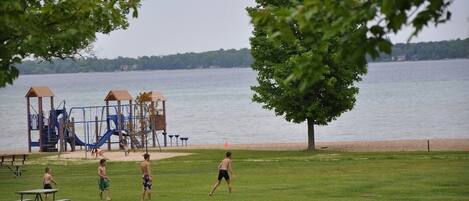 A playground with slides and swings, picnic tables, and a lake view.